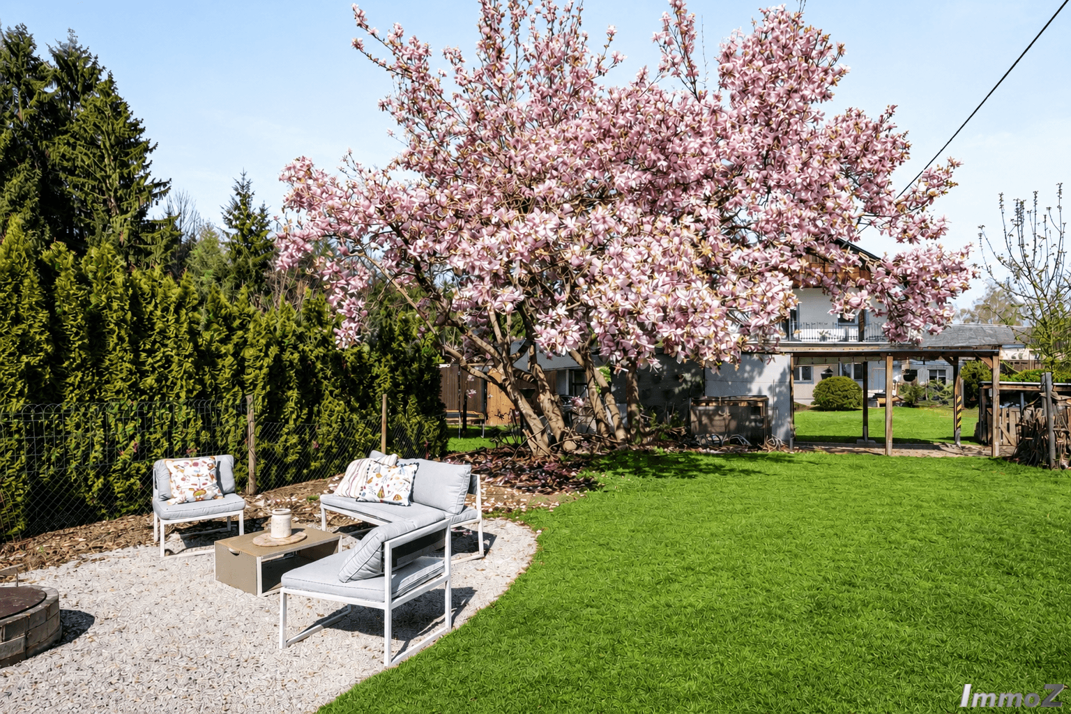 Sonniger Gartenbereich mit Sitzgelegenheiten, blühendem Baum und Kiesfläche für Entspannung.