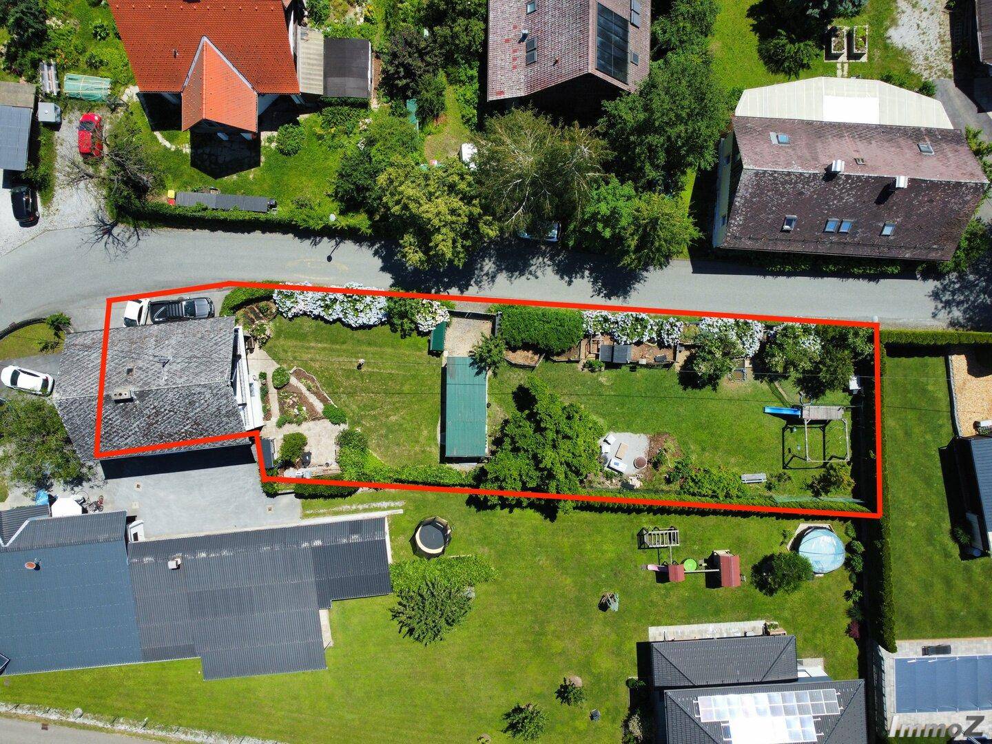 Luftaufnahme eines Grundstücks mit Haus und großem Garten, umrandet von einer roten Linie, inklusive Rasen und Pool.
