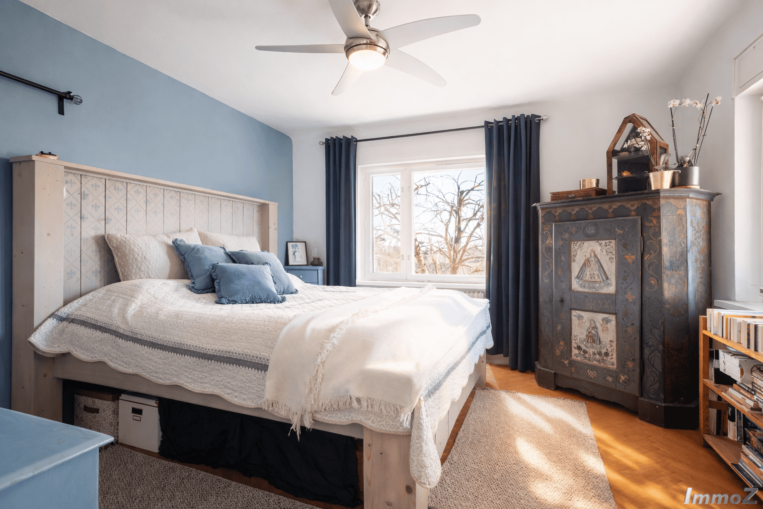 Geräumiges Schlafzimmer mit blau akzentuierter Wand, Holzbett und Deckenventilator.