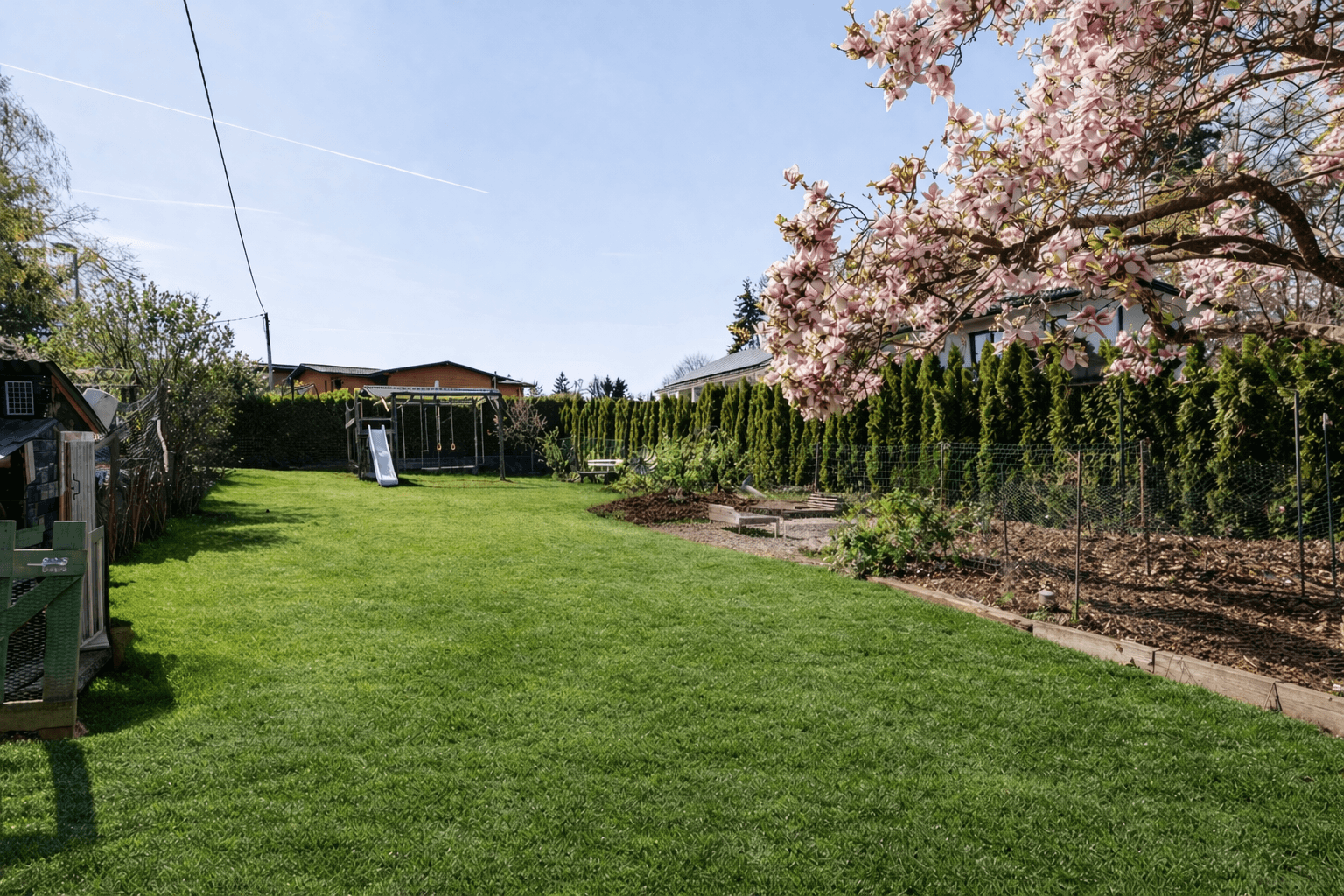 Großer, gepflegter Garten mit Rasenfläche, hohen Hecken und einem Spielbereich für Kinder.