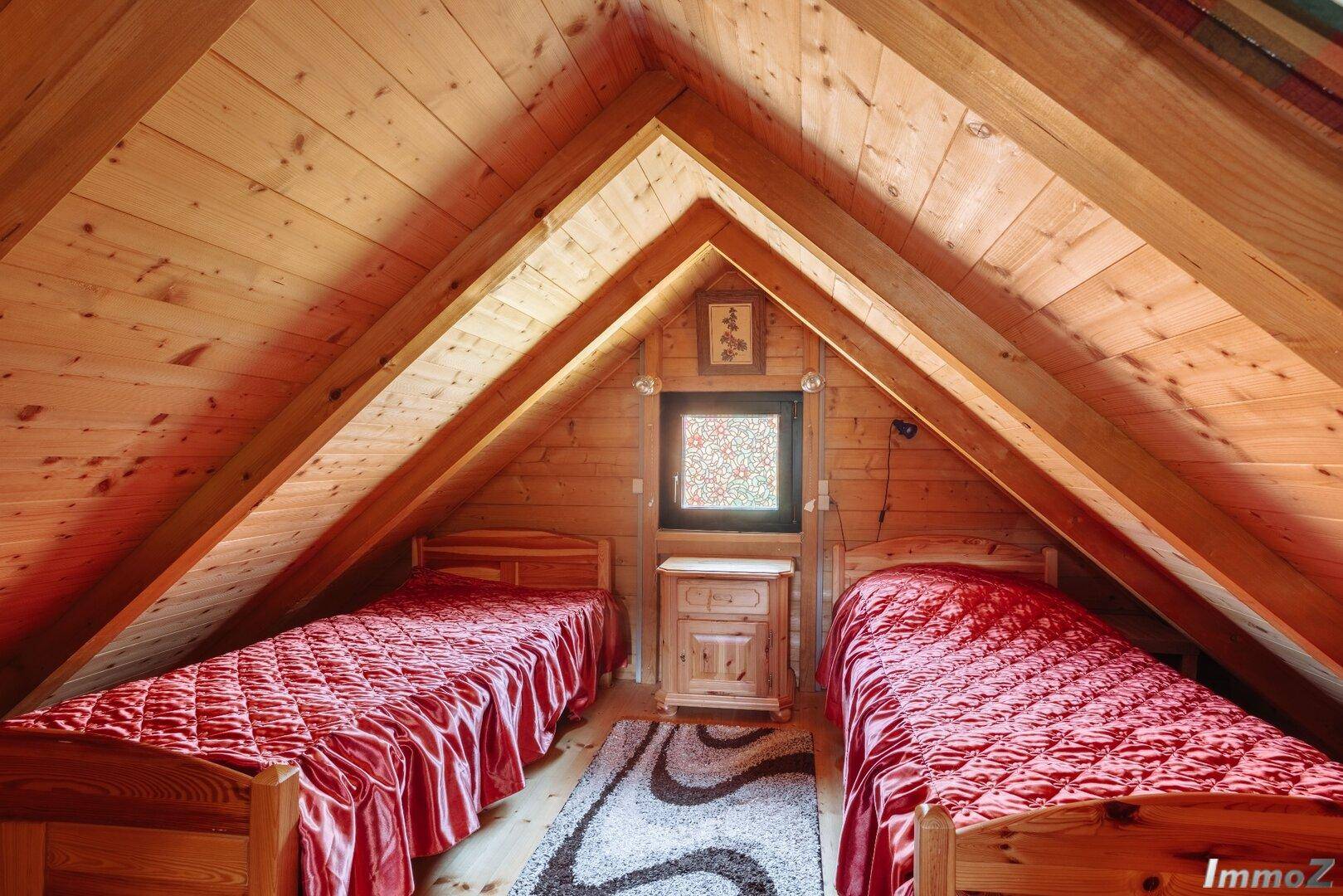 Schlafzimmer im Dachgeschoss mit zwei Einzelbetten, Holzvertäfelung und Dachschrägen.