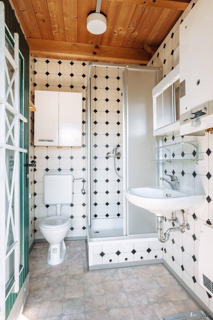 Kleines Badezimmer mit Dusche, WC und Waschbecken, gefliest in Schwarz-Weiß-Muster.