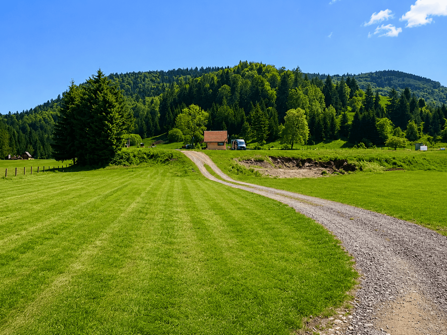 Idyllische Landschaft mit grünen Wiesen, bewaldeten Hügeln und einem Schotterweg zum Haus.