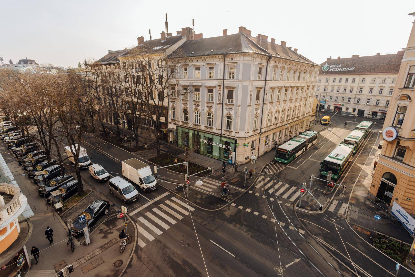 Luftaufnahme einer belebten Stadtkreuzung mit historischen Gebäuden, Fahrzeugen und öffentlichen Verkehrsmitteln.