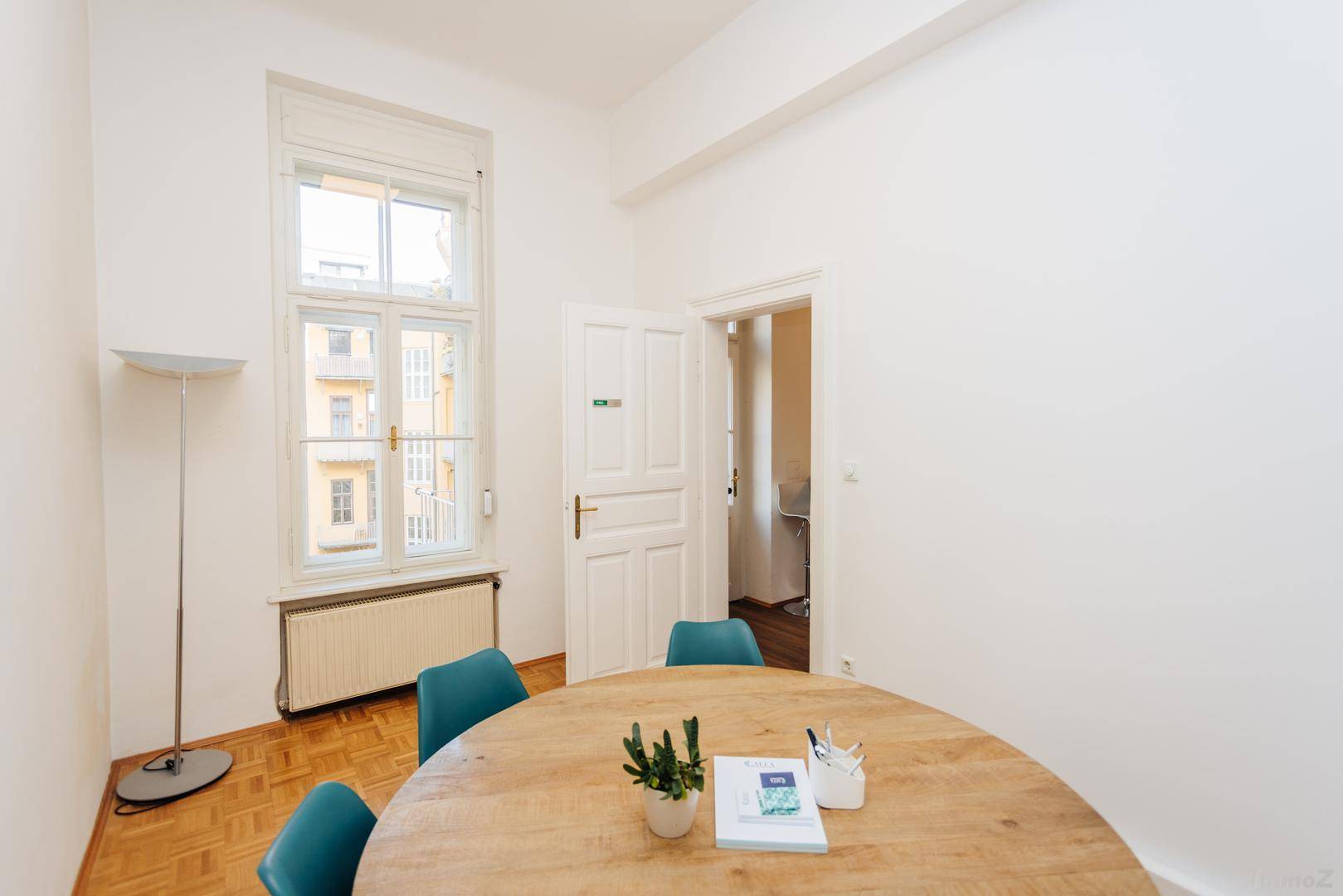 Heller Büroraum mit Holzboden, großem Fenster und einem runden Holztisch mit Stühlen.
