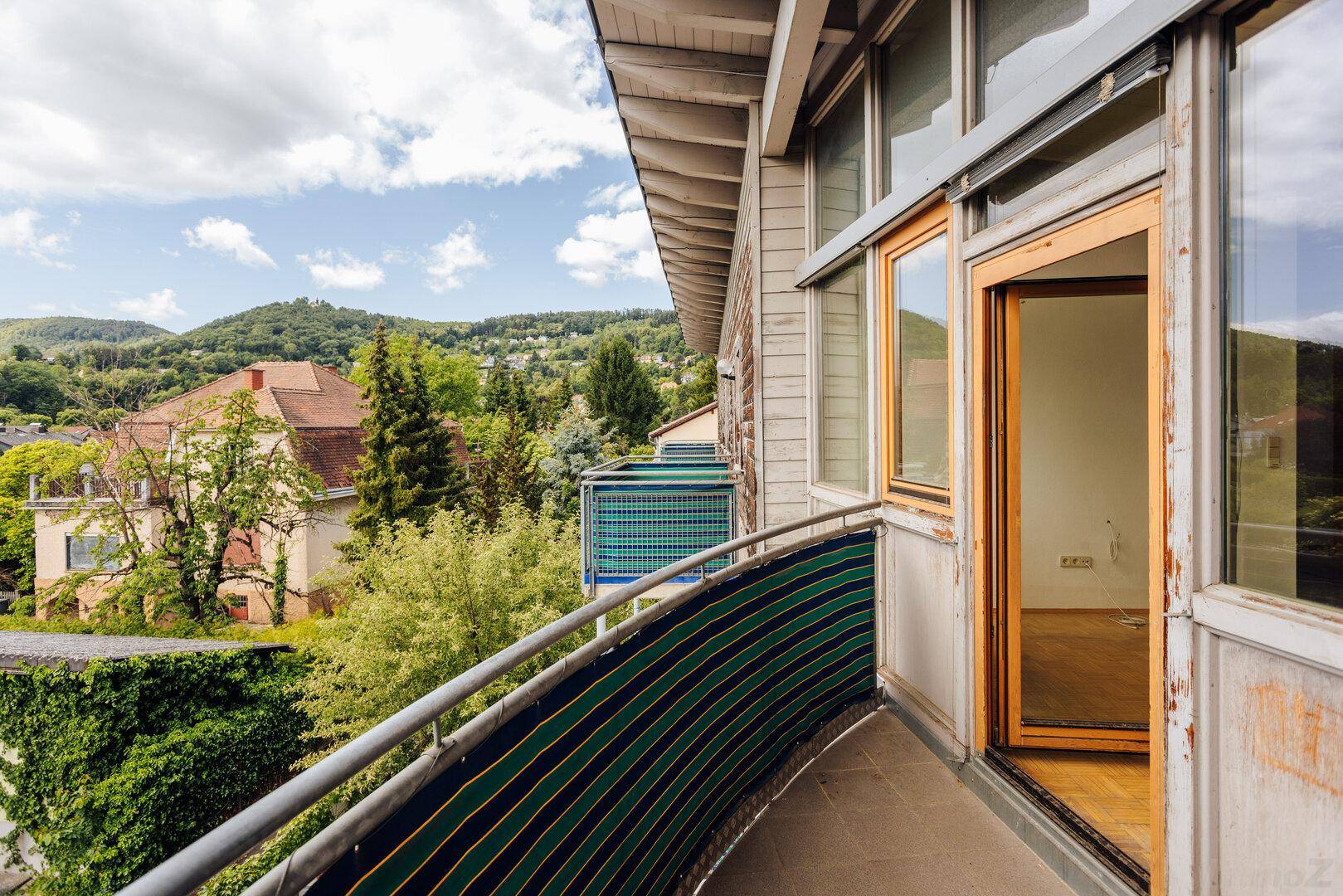 Gebogener Balkon mit Sichtschutz und Panoramablick auf die umliegende grüne Landschaft.