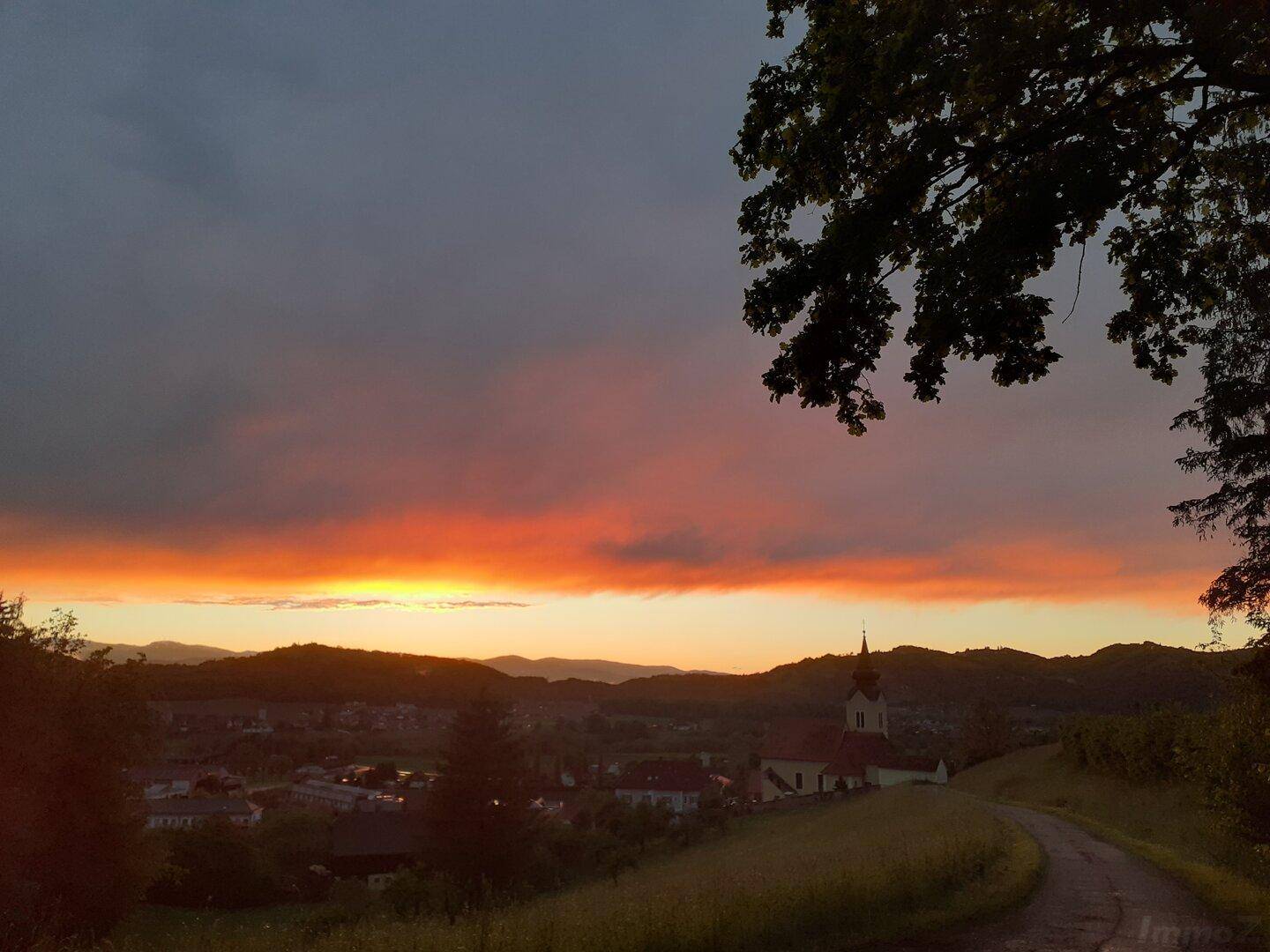 Spektakulärer Sonnenuntergang über einem Dorf und den umliegenden Hügeln mit leuchtendem Himmel.