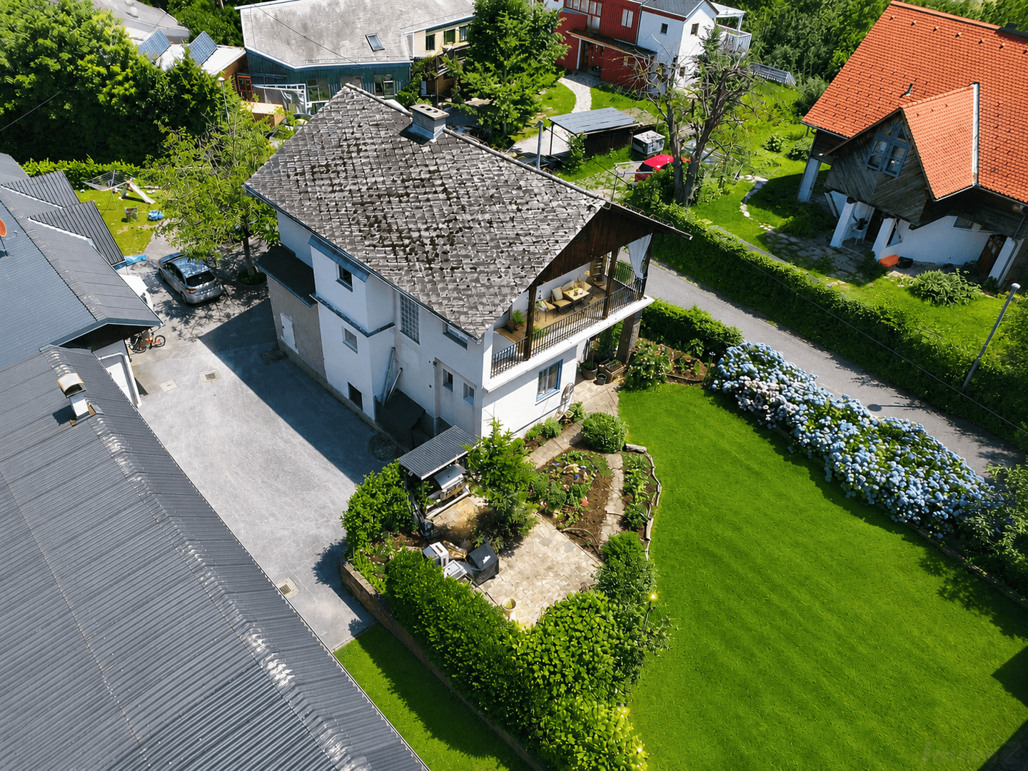 Luftaufnahme des Hauses mit großer gepflasterter Terrasse, Garten und angrenzendem Nebengebäude.