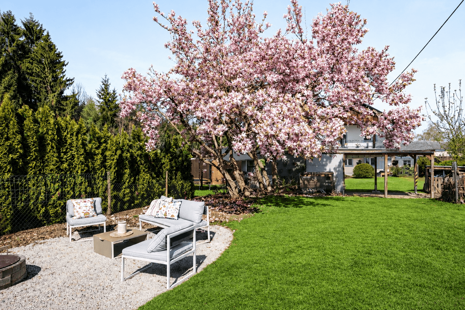 Gemütlicher Sitzbereich im Garten unter einem blühenden Baum mit modernen Gartenmöbeln.
