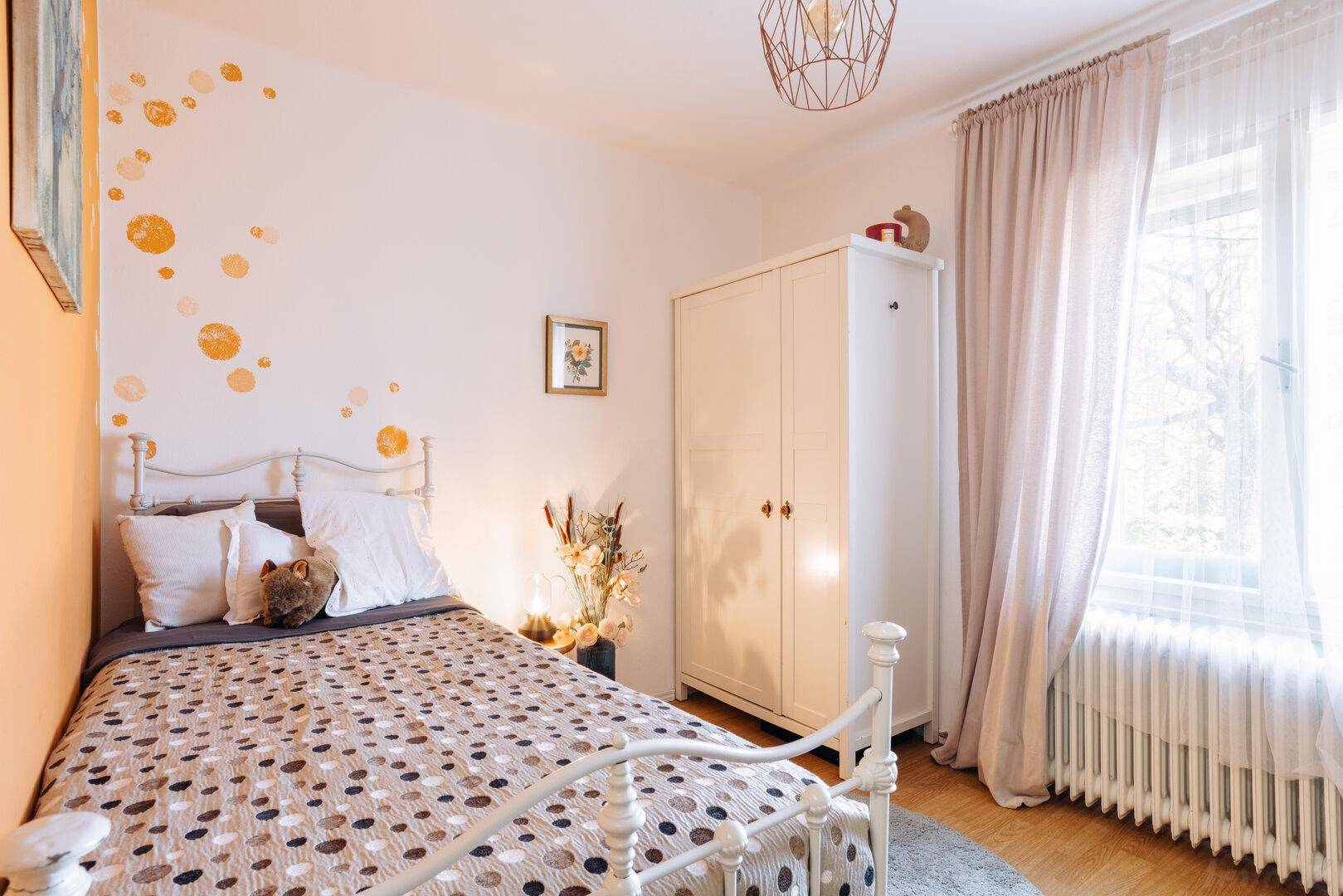 Helles Schlafzimmer mit Doppelbett, Holzboden und verspielter Wanddekoration.