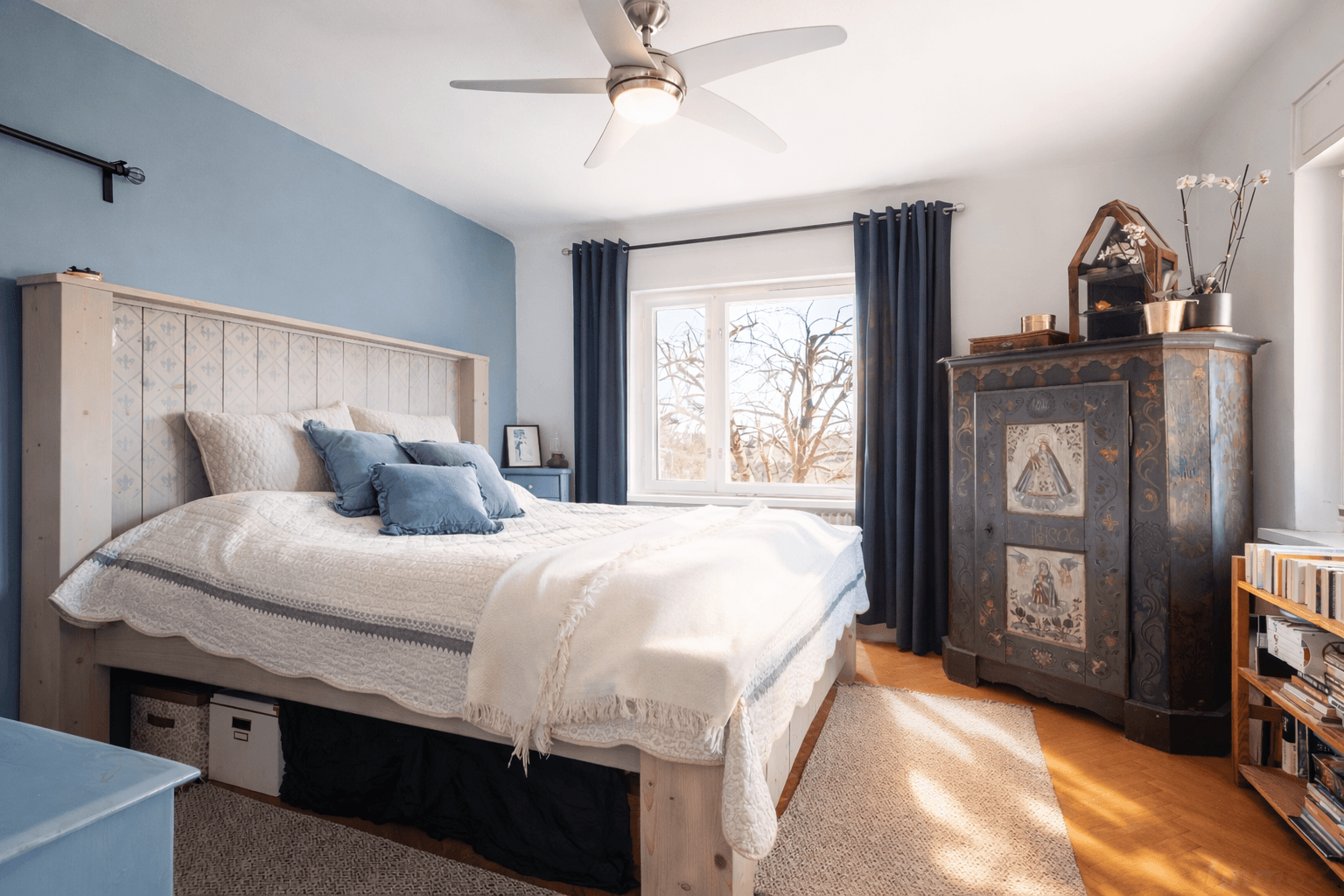 Geräumiges Schlafzimmer mit blau gestrichener Wand, Holzbett und antiker Kommode.