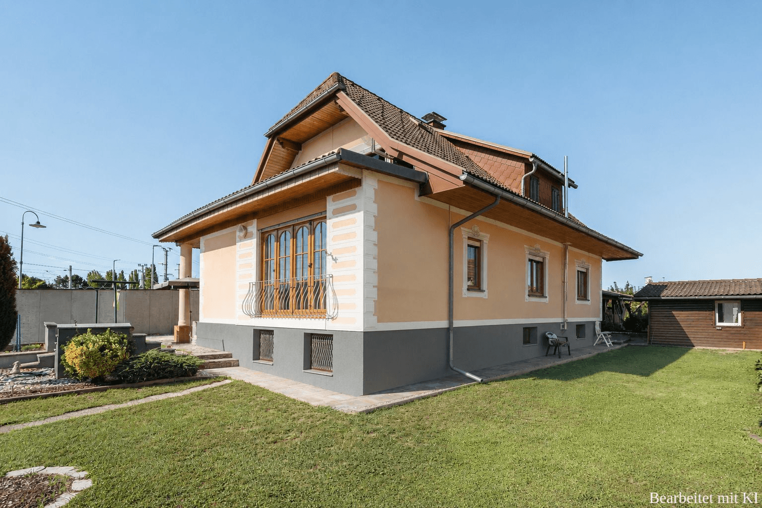 Seitenansicht des Hauses mit Balkon, gepflegtem Rasen und ländlicher Umgebung an einem sonnigen Tag.
