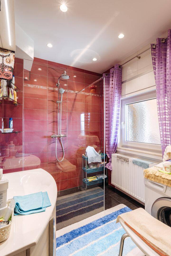 Modernes Badezimmer mit rotem Fliesenbereich, geräumiger Dusche und einem Fenster für Tageslicht.
