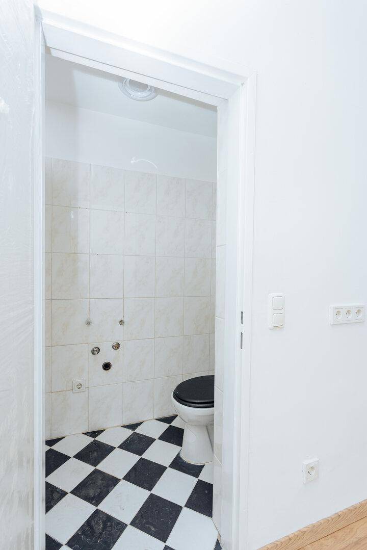 Kleines WC mit schwarz-weiß karierten Fliesen und weiß gefliesten Wänden, funktional eingerichtet.
