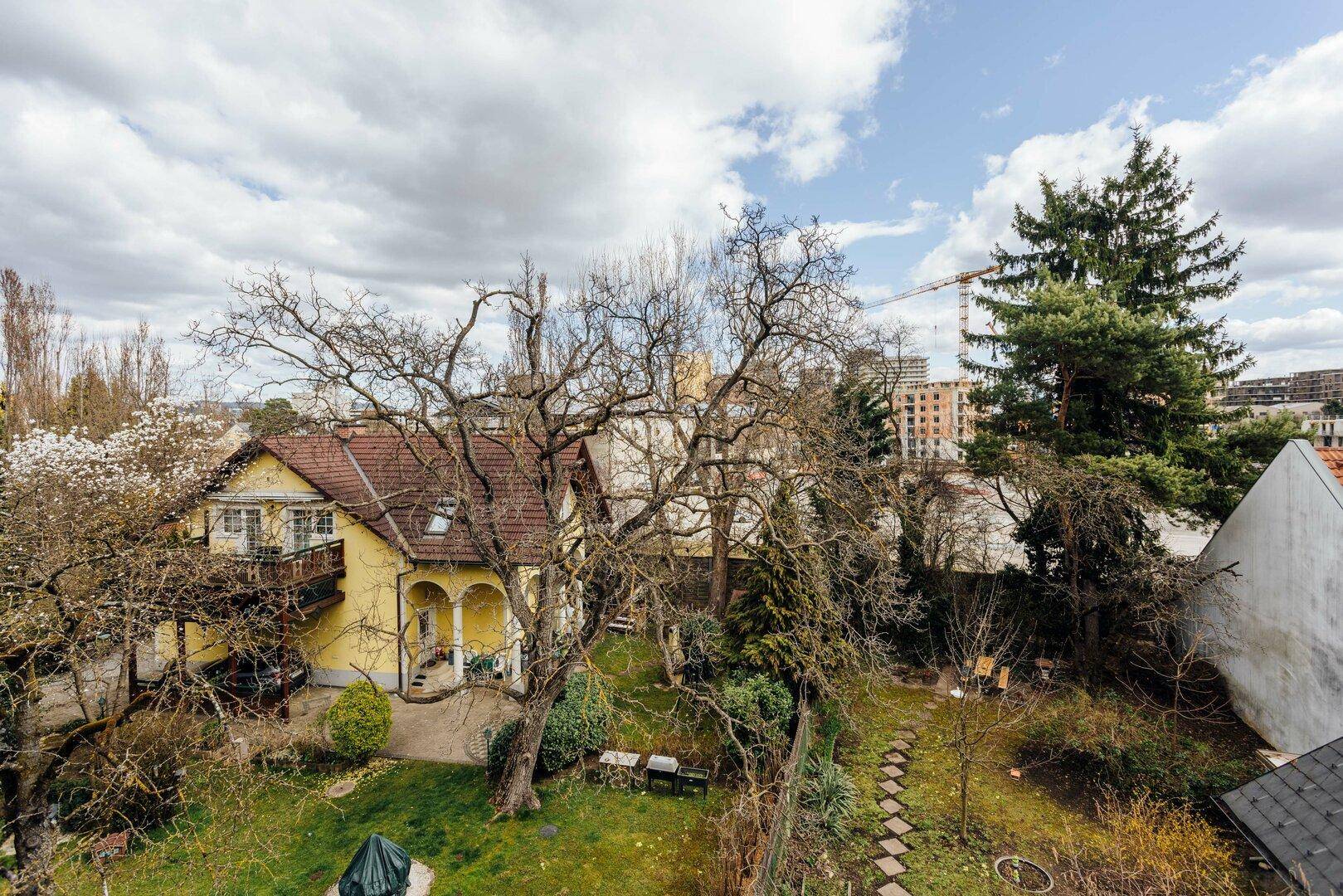 Vogelperspektive eines Hauses mit großem Garten, alten Bäumen und angrenzenden Gebäuden.