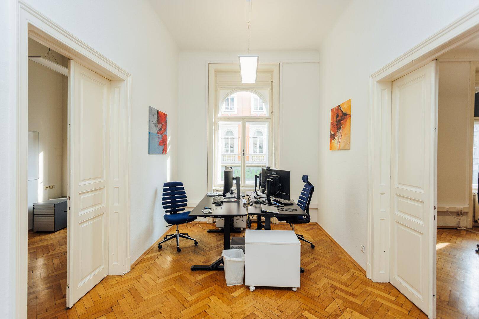 Helles Büro mit einem Schreibtisch, zwei Stühlen und zwei großen Türen zu angrenzenden Räumen.