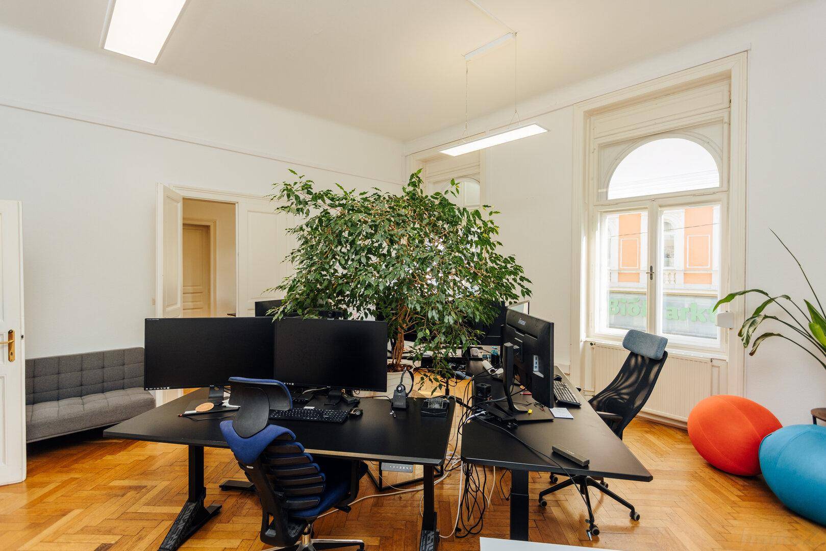 Modernes Büro mit mehreren Arbeitsplätzen, bequemen Sitzgelegenheiten und großen Fenstern.
