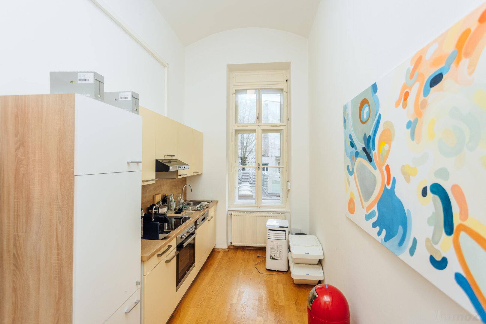 Helle Küchenzeile mit modernen Geräten, Holzarbeitsplatte und einem farbenfrohen Kunstwerk.