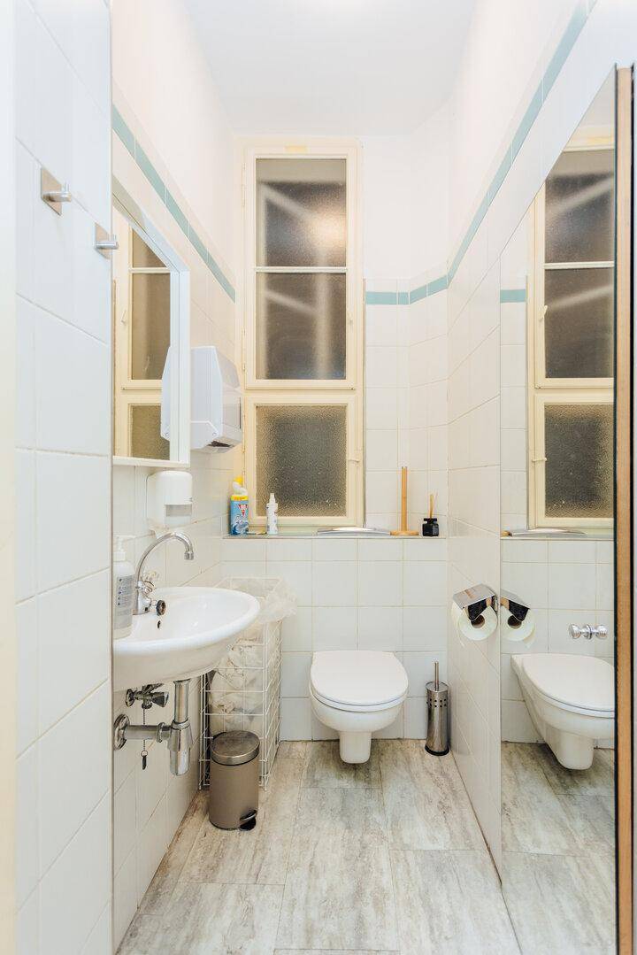 Helles Badezimmer mit WC, Waschbecken, Fenster und weißen Fliesen.