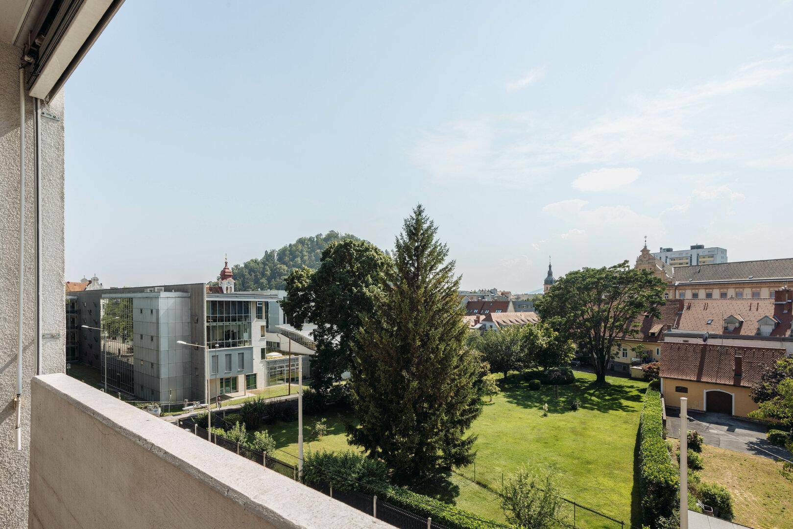 Panoramablick über eine grüne Landschaft mit Bäumen und städtischer Bebauung.