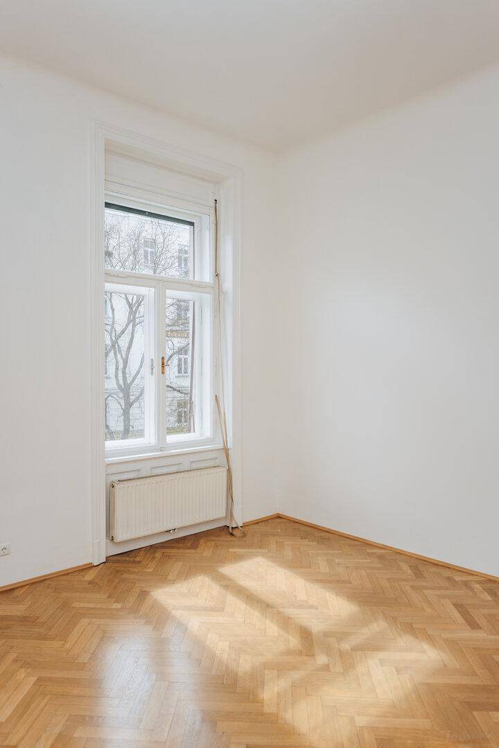 Heller Raum mit Fischgrätparkett, einem hohen Fenster und Sonneneinstrahlung auf dem Boden.