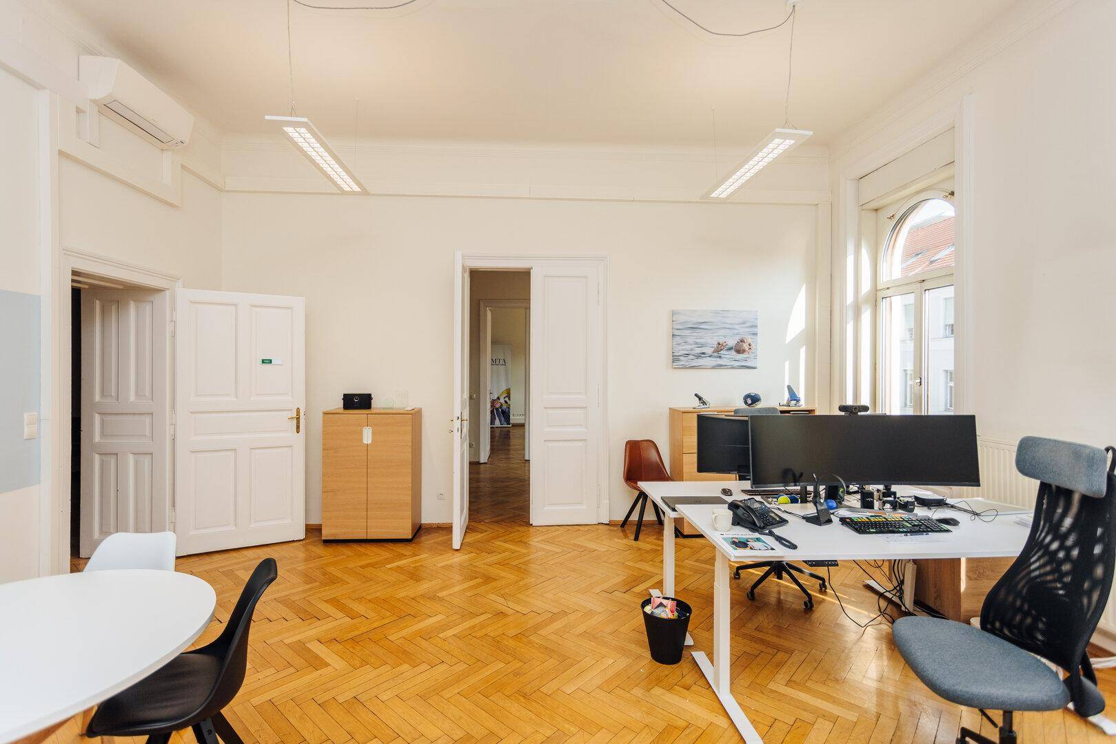 Büro mit Fischgrätparkett, Schrank und Blick durch die Tür in einen weiteren Raum.