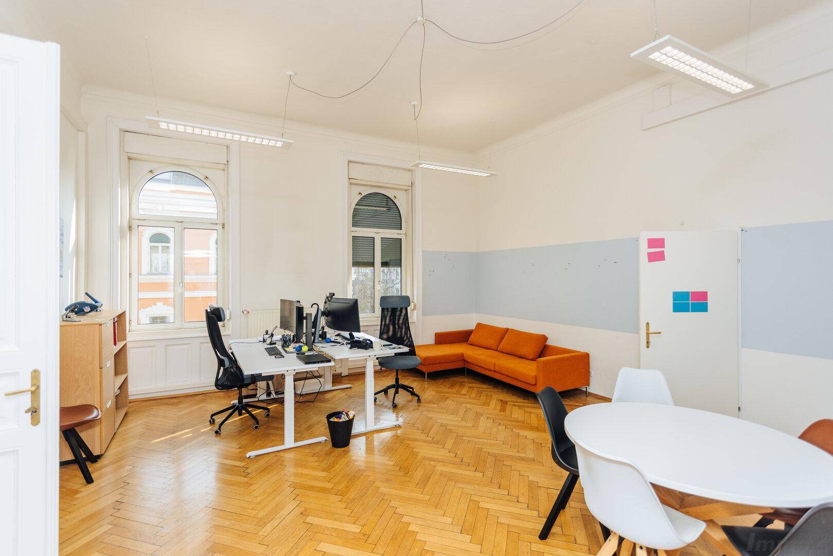 Großes Büro mit Fischgrätparkett, Sitzbereich und mehreren Arbeitsplätzen.