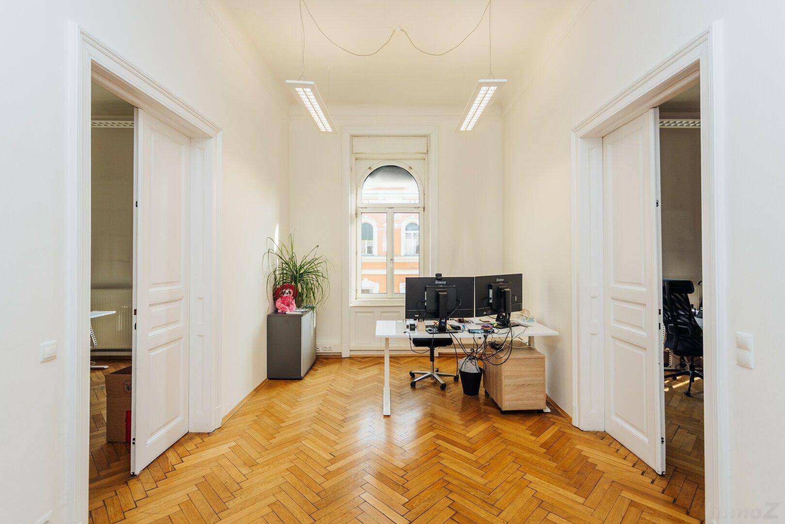 Büro mit Fischgrätparkett, Fenster und zwei offenen Türen zu weiteren Räumen.