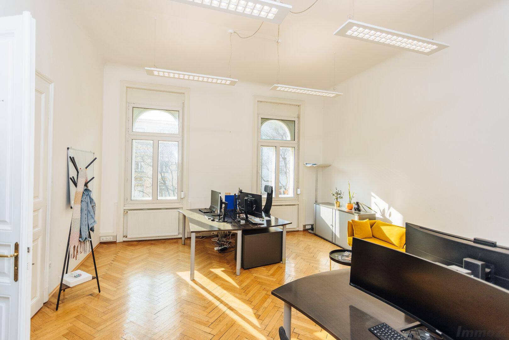 Großes Büro mit Fischgrätparkett, viel Tageslicht und mehreren Arbeitsplätzen.