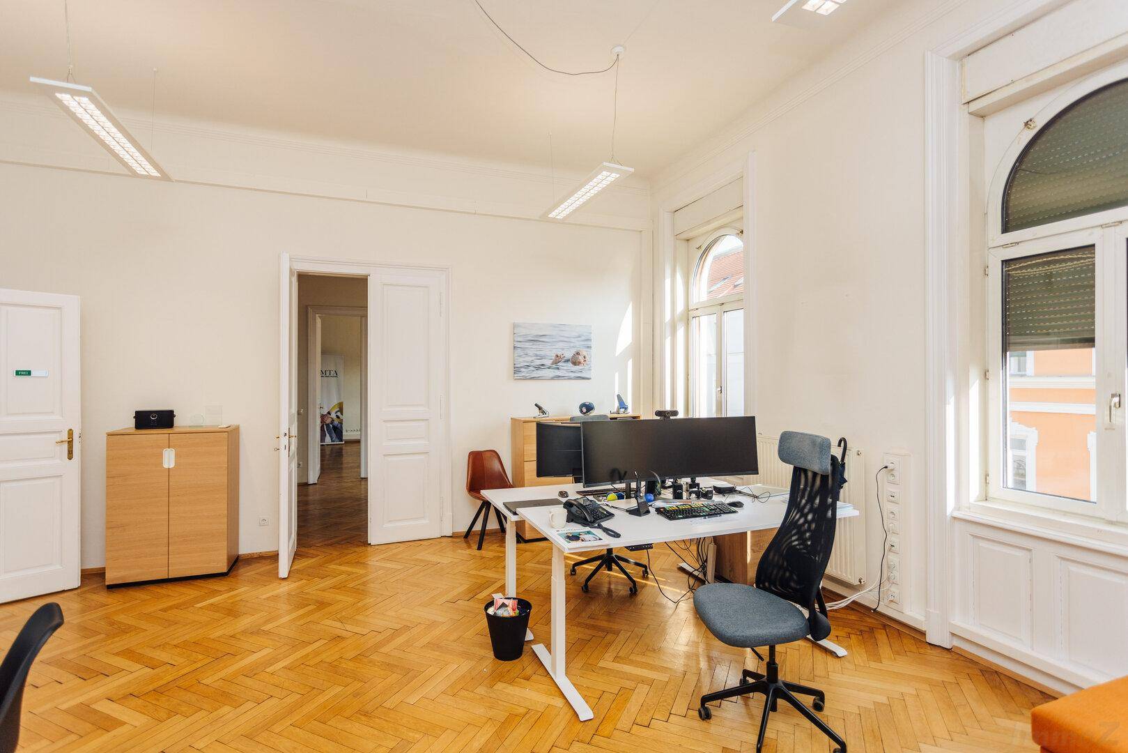 Geräumiges Büro mit Fischgrätparkett, großen Fenstern und modernen Arbeitsplätzen.