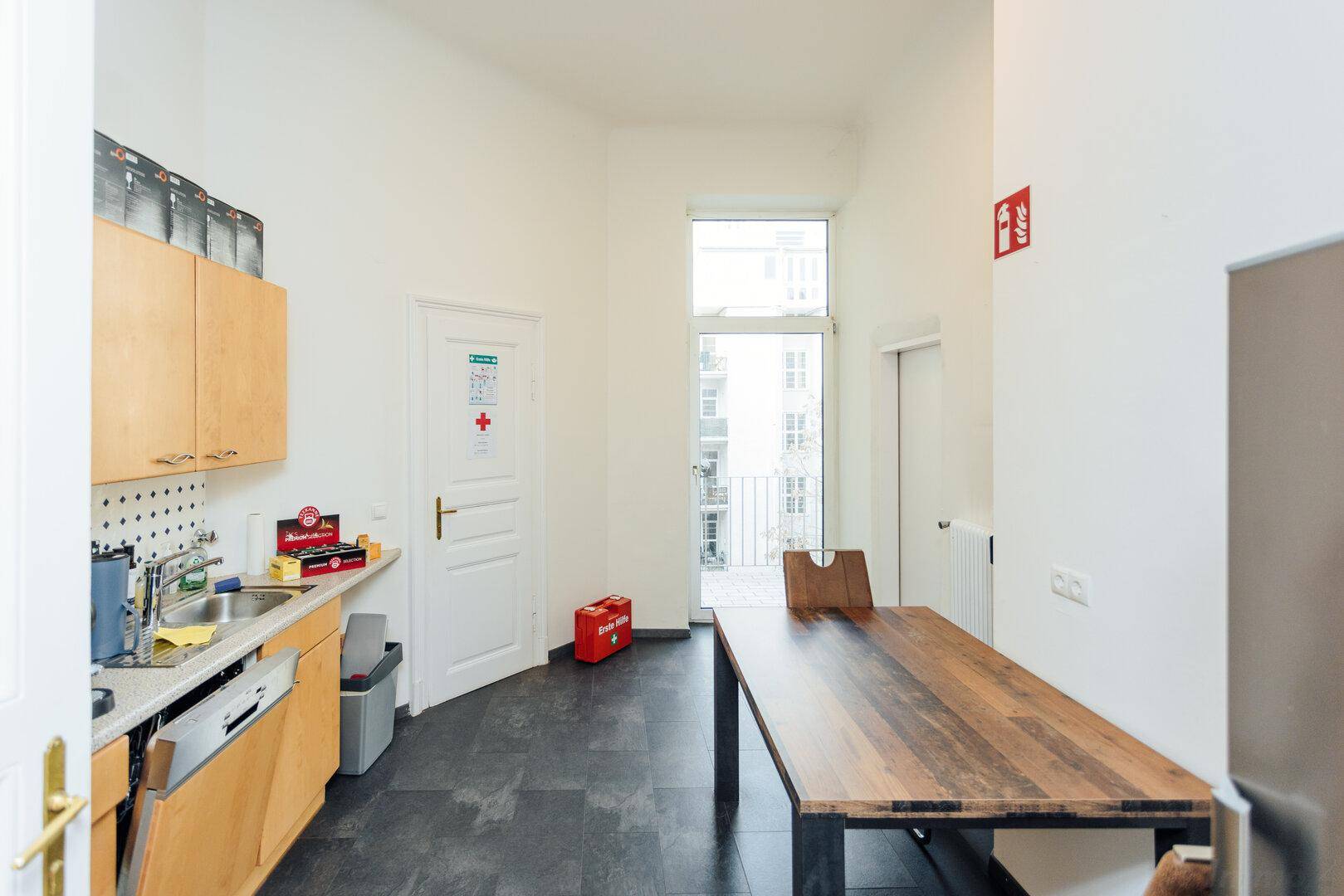 Helle Küche mit Holztisch, dunklem Fliesenboden und Zugang zu einem kleinen Balkon.