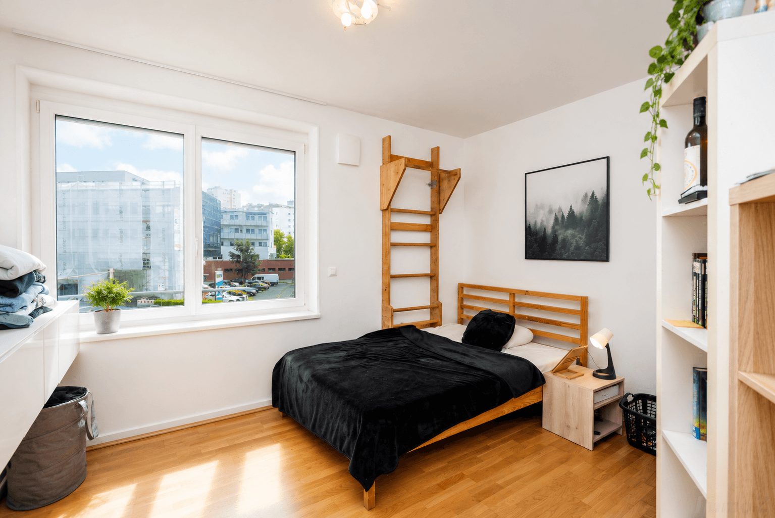 Helles Schlafzimmer mit Holzbett, Sprossenwand und Blick auf die Stadt.