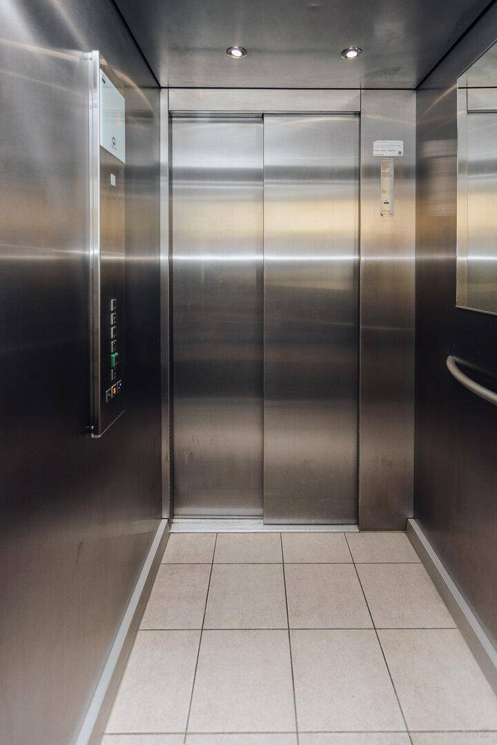 Moderner Aufzug mit Edelstahloberflächen und Fliesenboden im Gebäude.