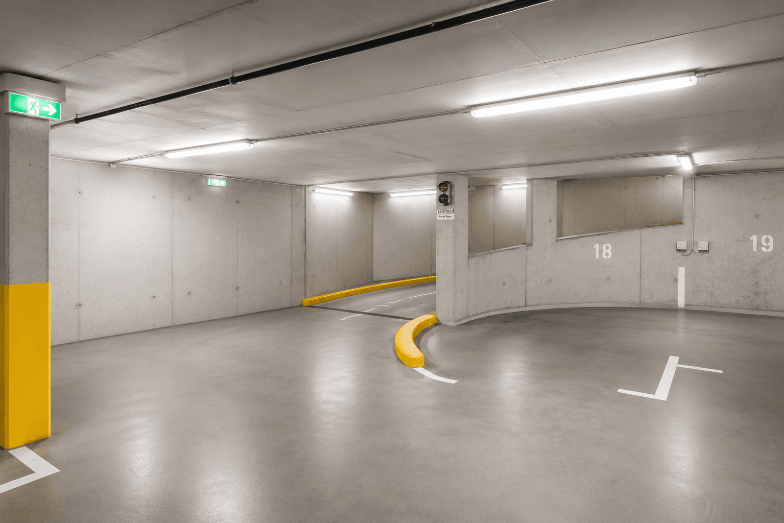 Geräumige Tiefgarage mit Betonwänden, hellen Leuchten und markierten Parkplätzen.