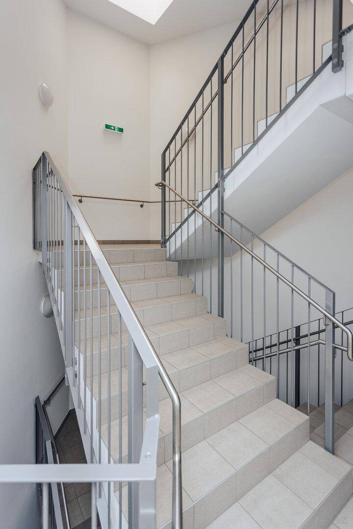 Helles Treppenhaus mit Fliesenboden und Metallgeländer in einem Mehrfamilienhaus.