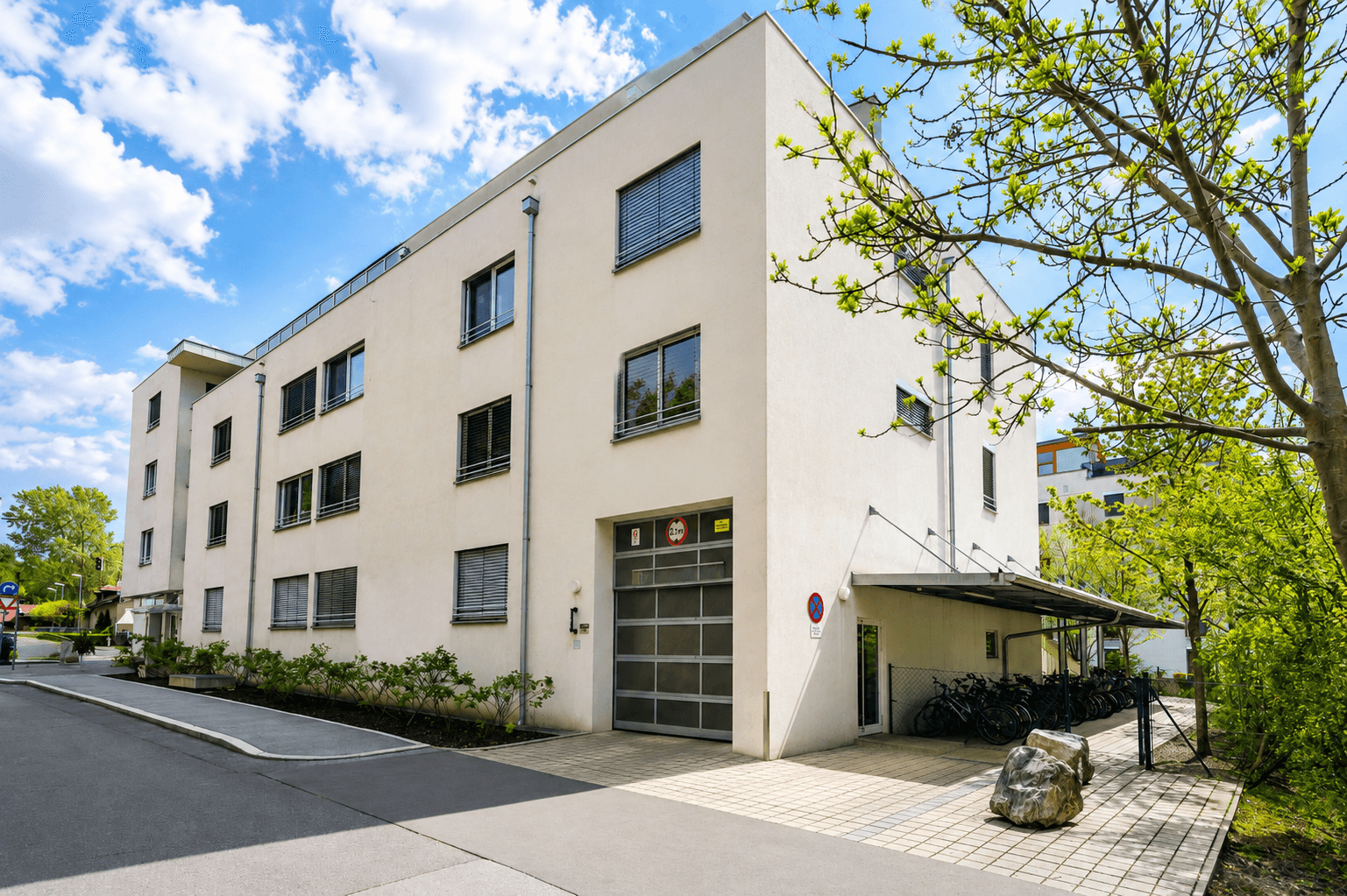 Modernes Mehrfamilienhaus mit schlichter Fassade, großen Fenstern und Fahrradabstellplatz.