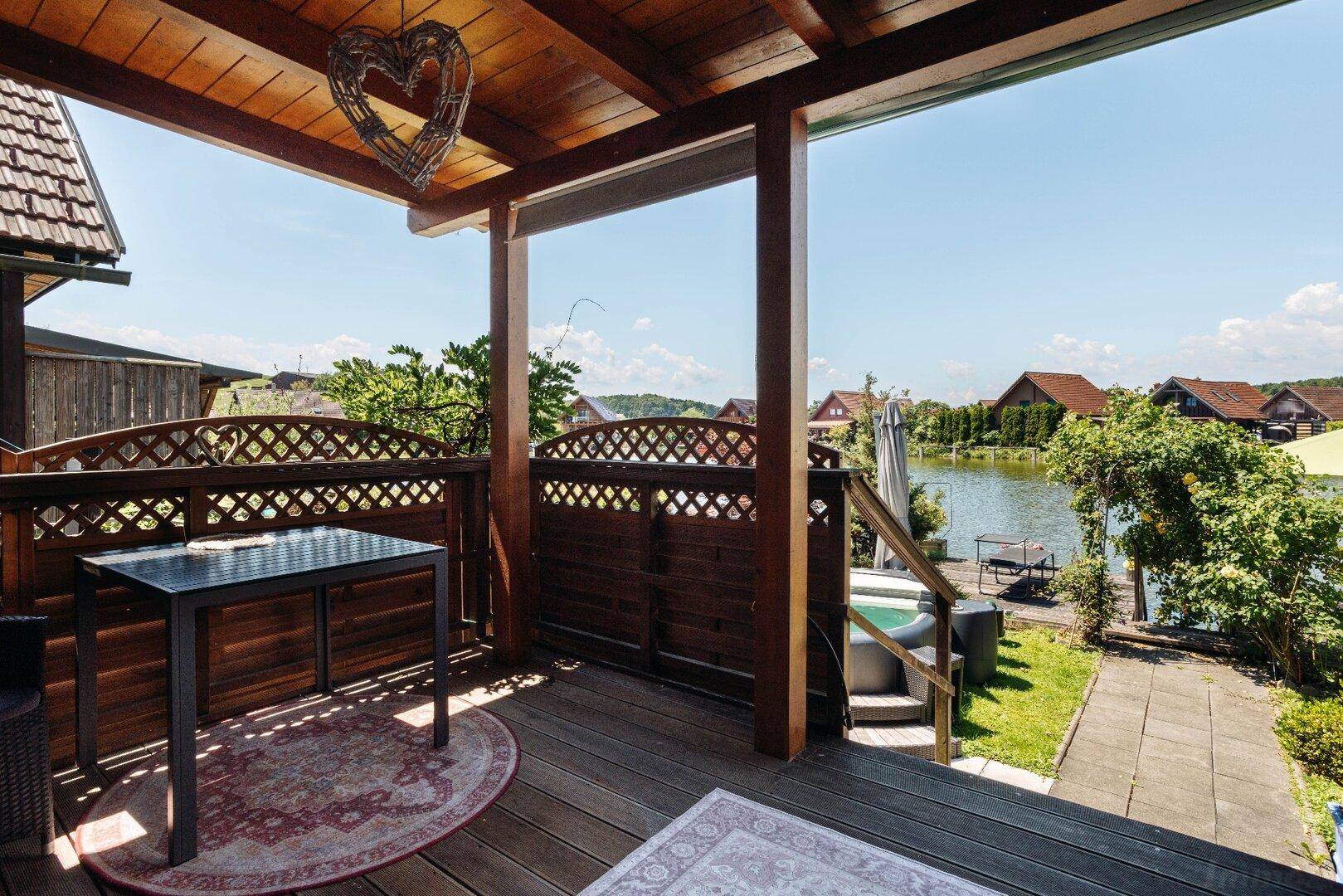 Überdachter Balkon mit Holzboden und Gittergeländer, bietet einen schönen Blick auf den See.