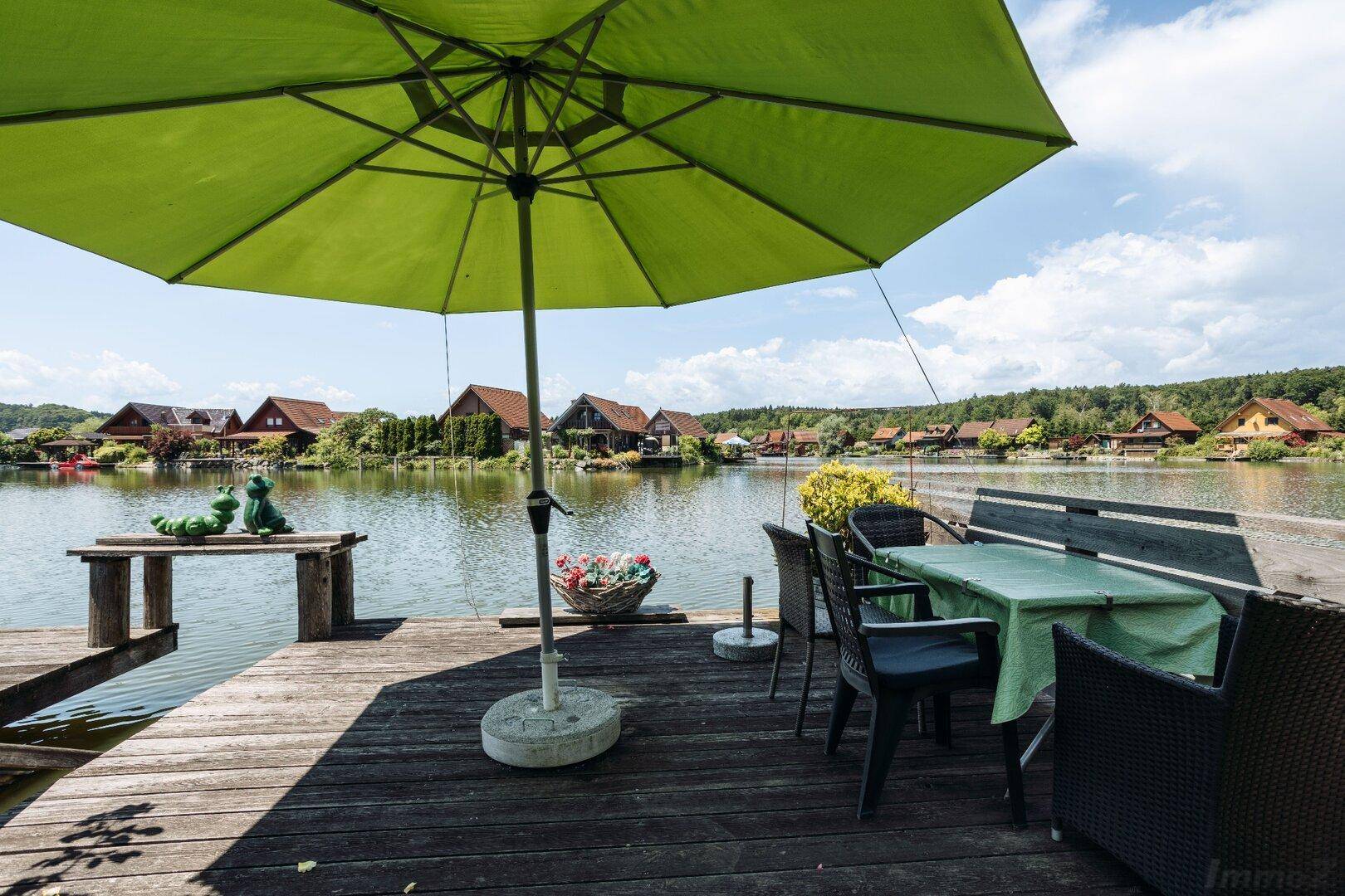 Gemütliche Holzterrasse direkt am See mit Esstisch und Sonnenschirm, ideal zum Entspannen.