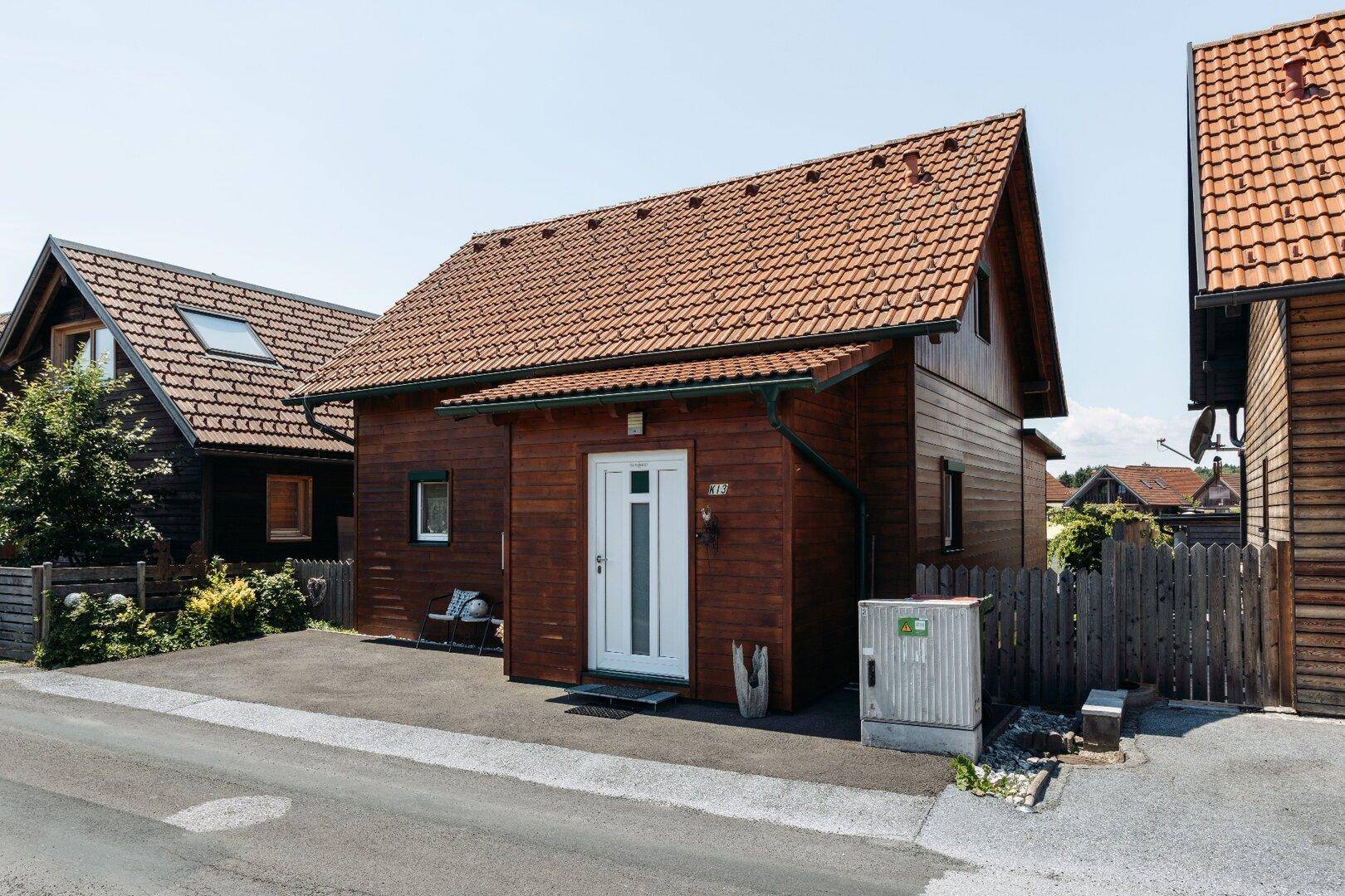 Ansicht des Holzhauses von der Straßenseite mit Eingangsbereich und gepflasterter Zufahrt.