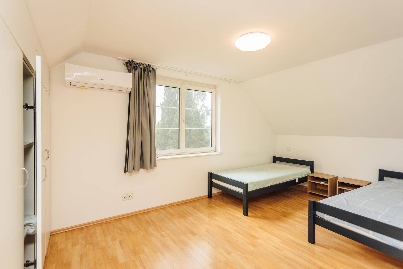 Helles Schlafzimmer mit zwei Einzelbetten, Klimaanlage und Fenster.