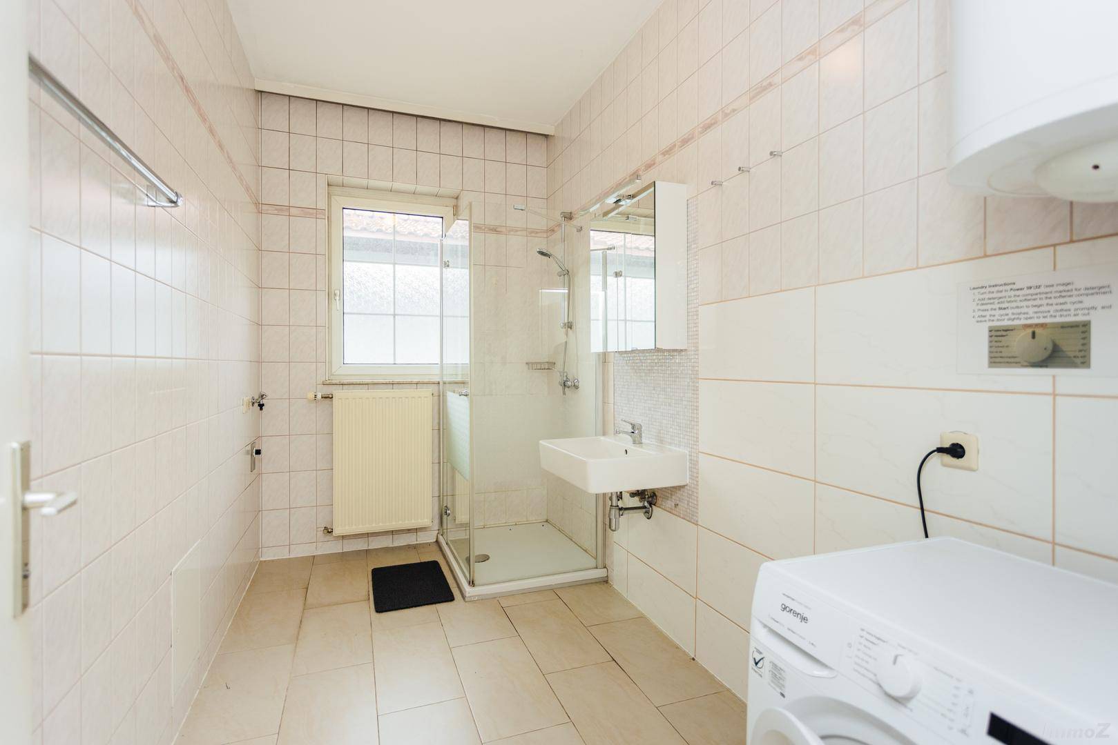 Badezimmer mit Dusche, Waschbecken, Waschmaschine und Fenster.