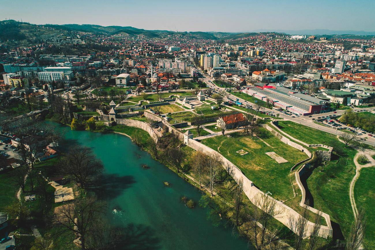 Panoramische Luftaufnahme einer Stadt mit Fluss, historischen Festungsanlagen und urbaner Bebauung.