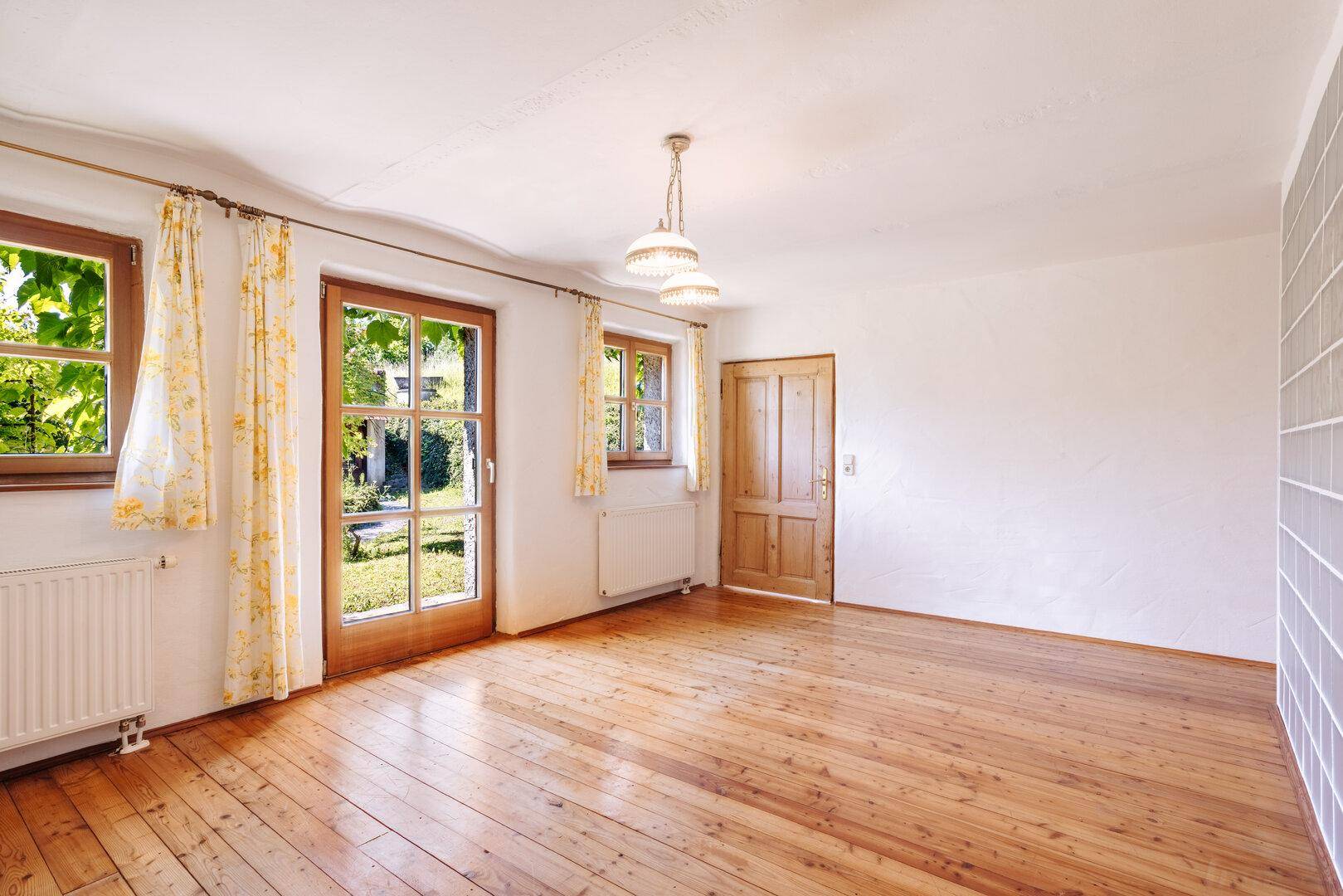 Geräumiger Raum mit Holzdielenboden und zwei Fenstertüren, die Zugang zum Außenbereich bieten.