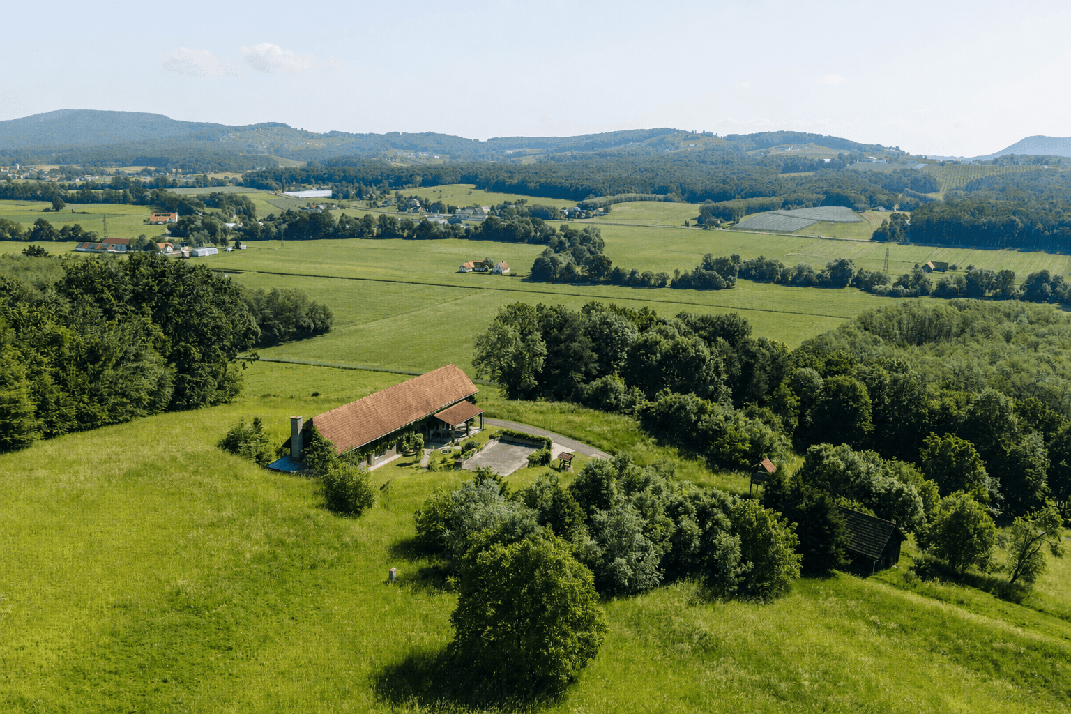 Weitläufige Luftaufnahme des Anwesens mit dem langen Gebäude, umgeben von grünen Feldern und Wäldern.