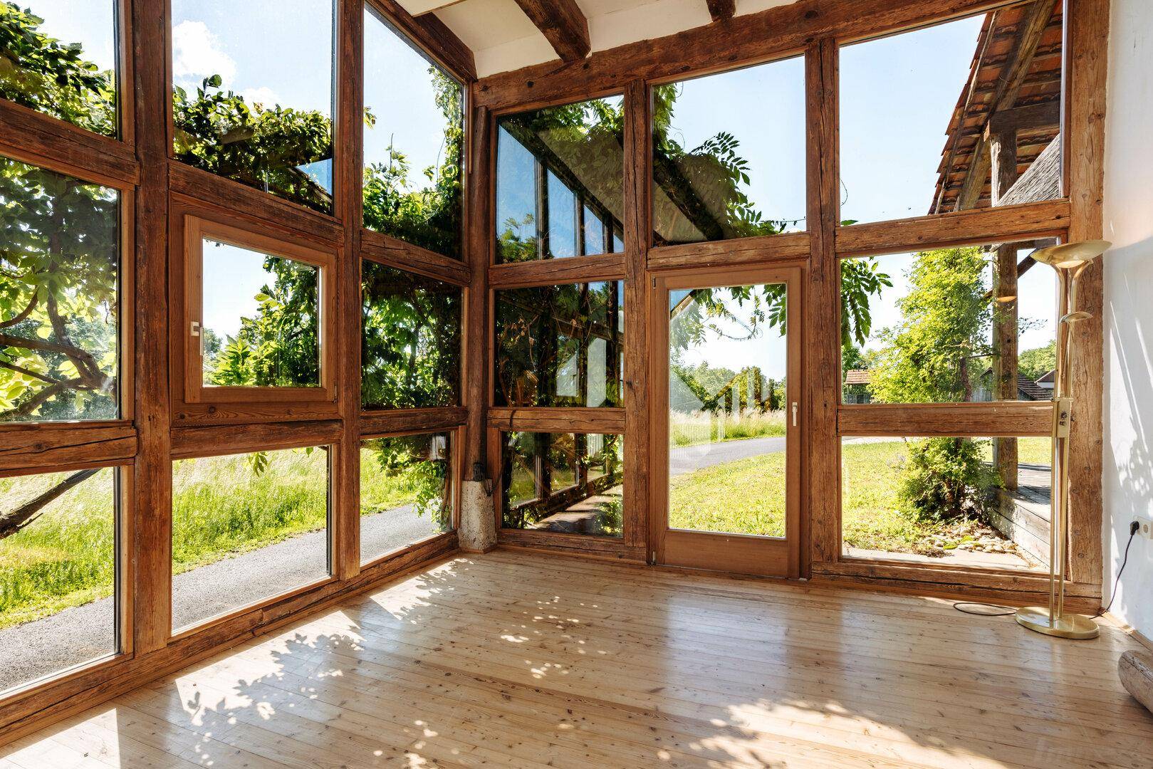 Heller Wintergarten mit Holzbalken und großen Fenstern bietet einen schönen Blick ins Grüne.