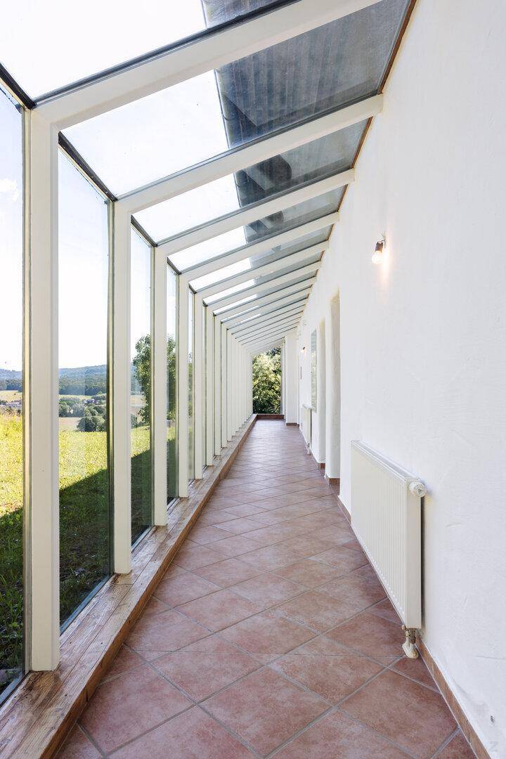 Heller Wintergarten mit Terrakottafliesen und weitem Blick über die grüne Landschaft.