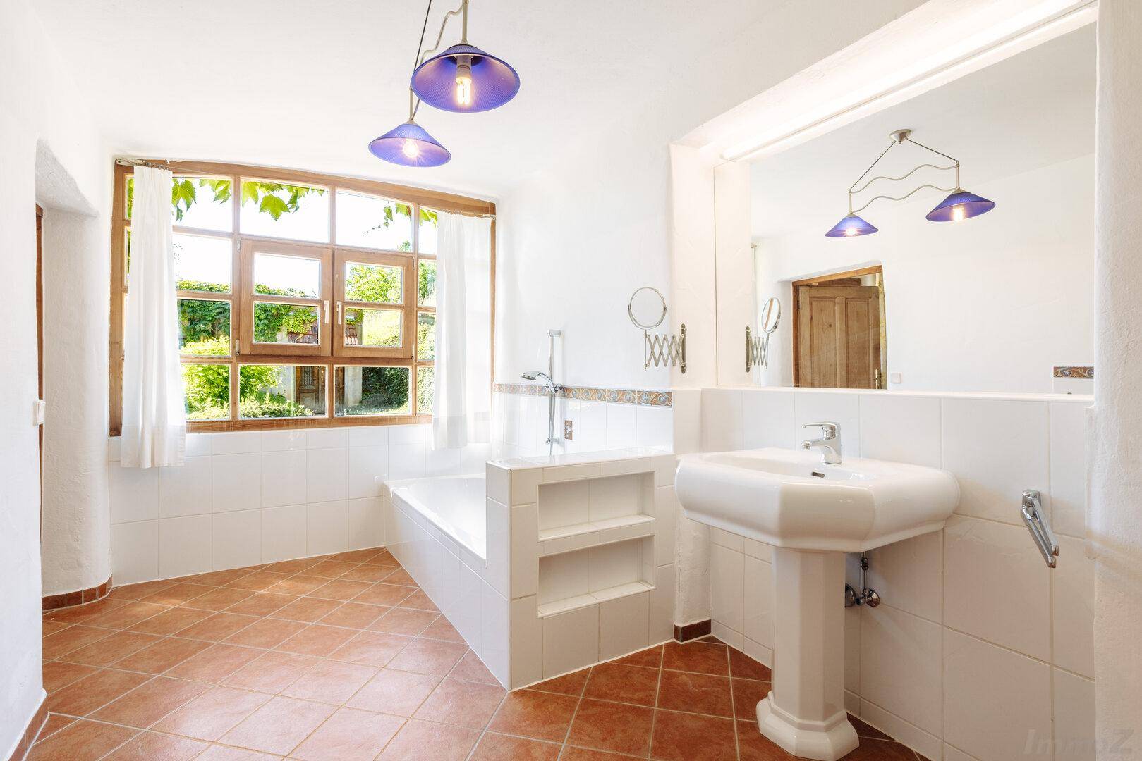 Helles Badezimmer mit Badewanne, Einzelwaschbecken und Fenster mit Blick in den Garten.