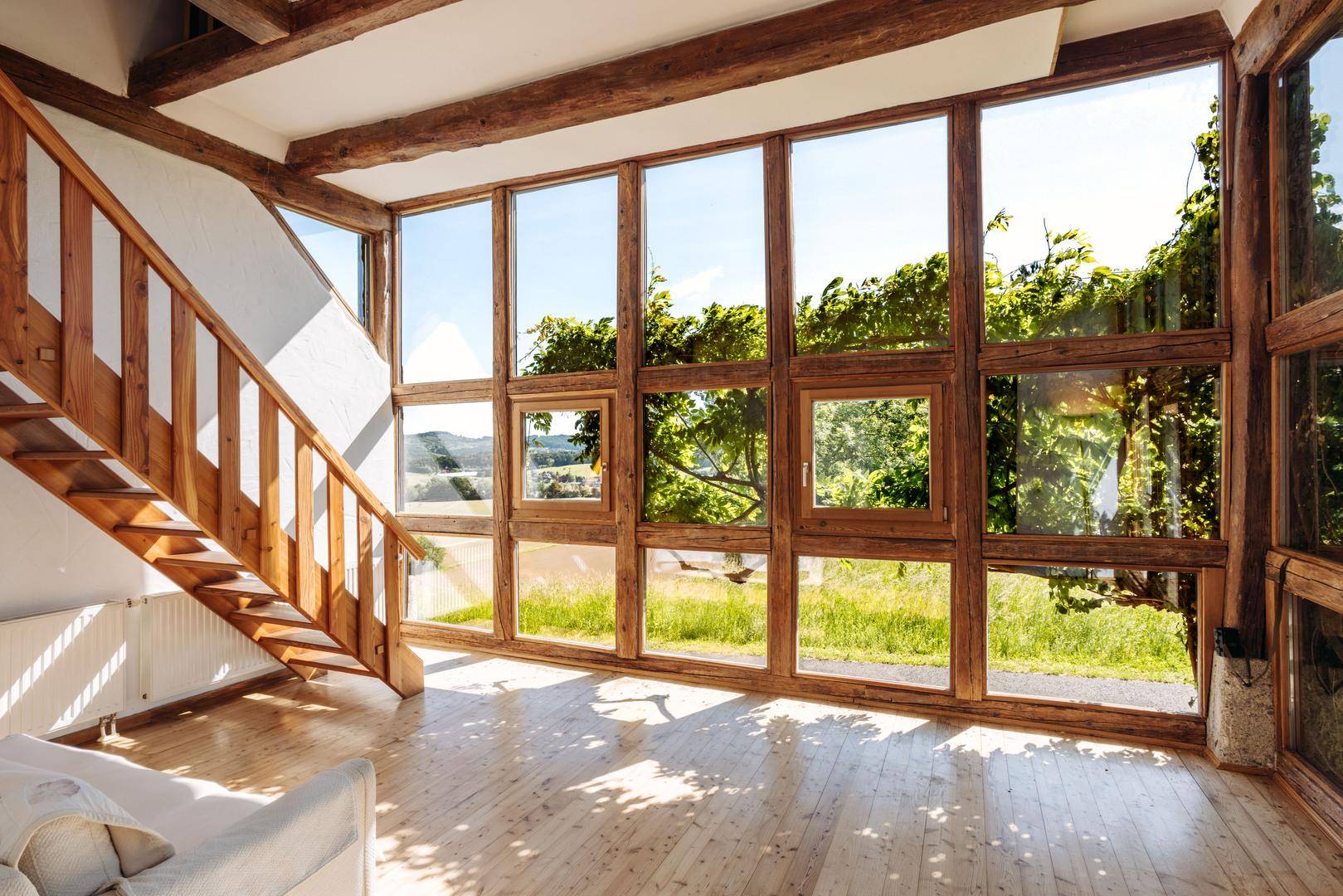 Heller Wohnbereich mit Holztreppe, großen Fenstern und weitem Blick ins Grüne.