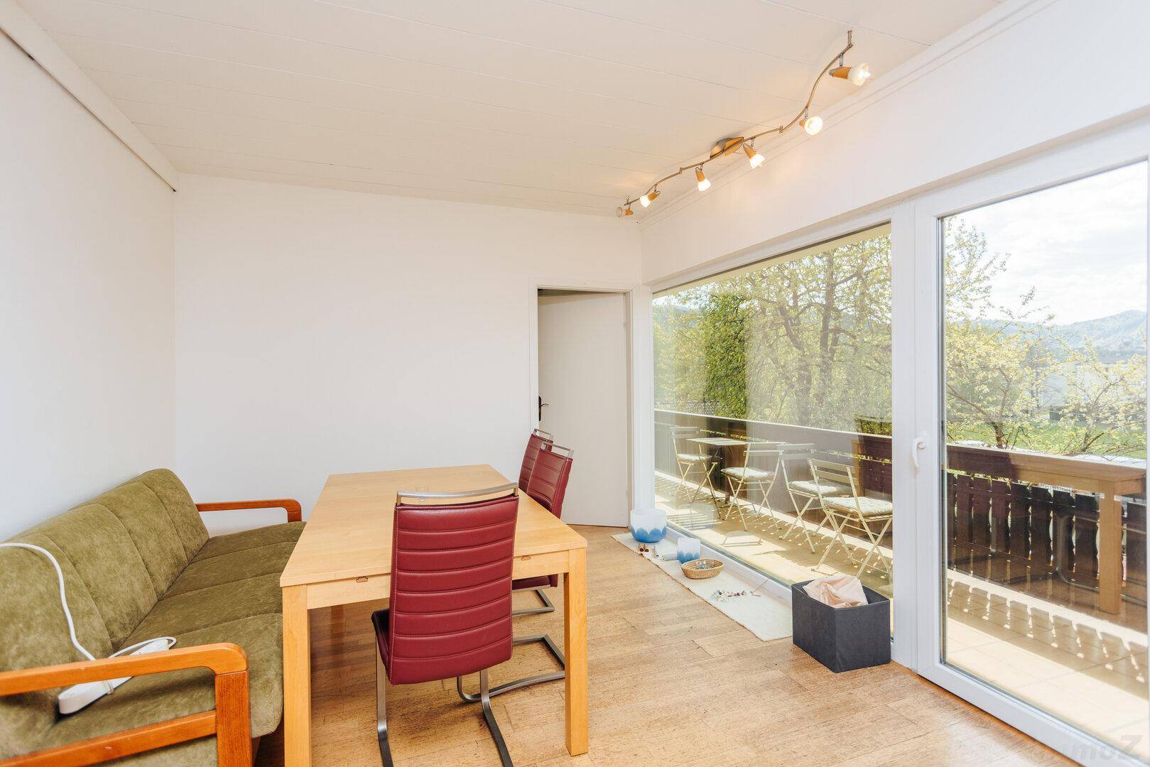 Heller Wohn- und Essbereich mit Holzboden und großem Fenster mit Zugang zum Balkon.