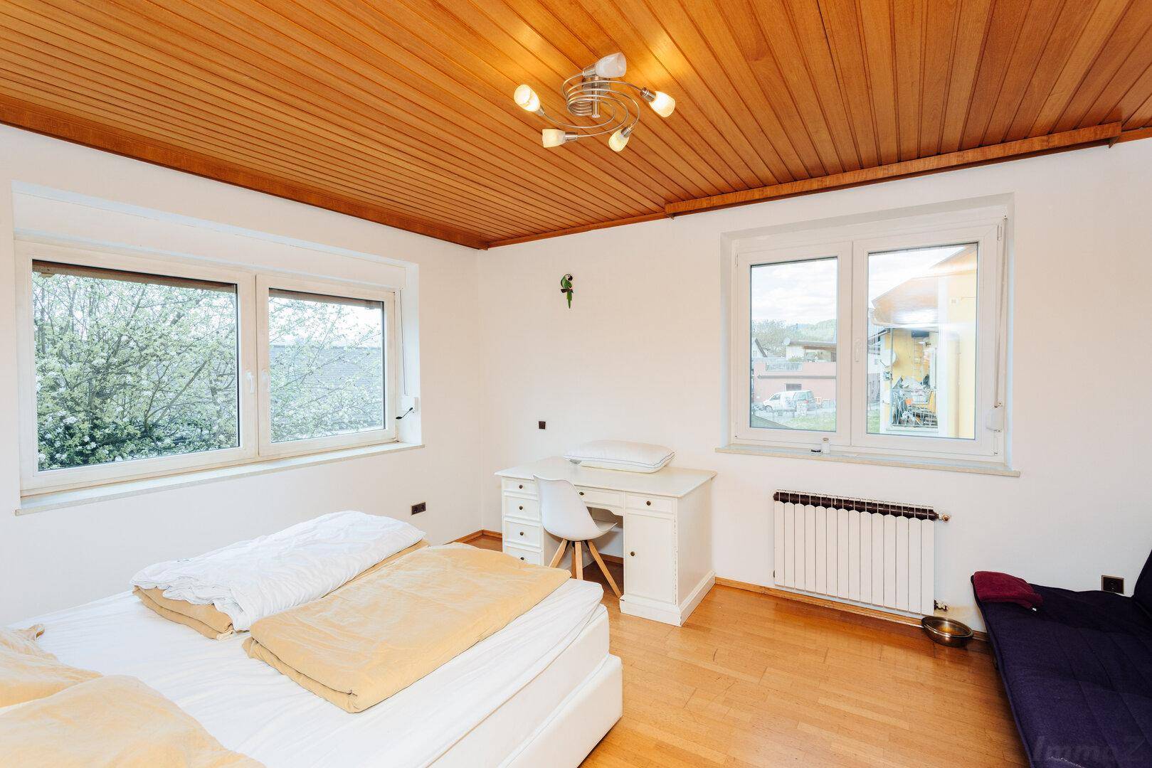 Gemütliches Schlafzimmer mit Holzboden, Holzdecke und zwei Fenstern für viel Tageslicht.